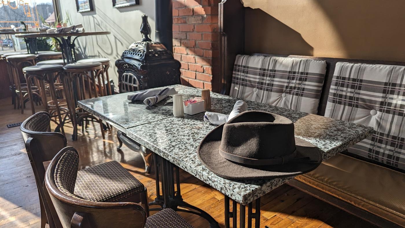 The dining room in low afternoon sun: exposed brick, an antique cast iron stove, bentwood cafe chairs and speckled stone bistro tables on ornate iron bases.